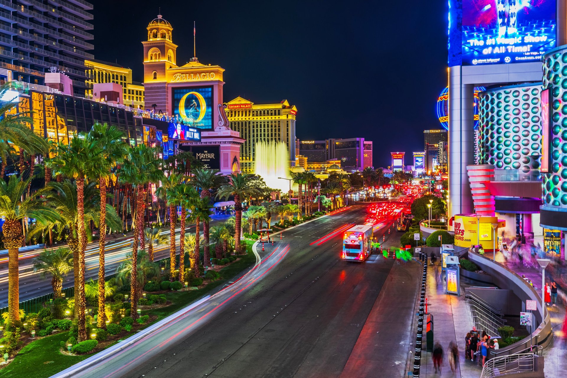 Light trails from cars on the Las Vegas Strip at night with palm trees and Bellagio in colorful neon lights