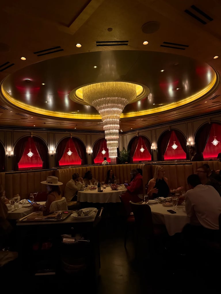 Elegant upscale restaurant interior with tiered circular ceiling, golden ring lighting, red booth seating, and crystal chandelier centerpiece