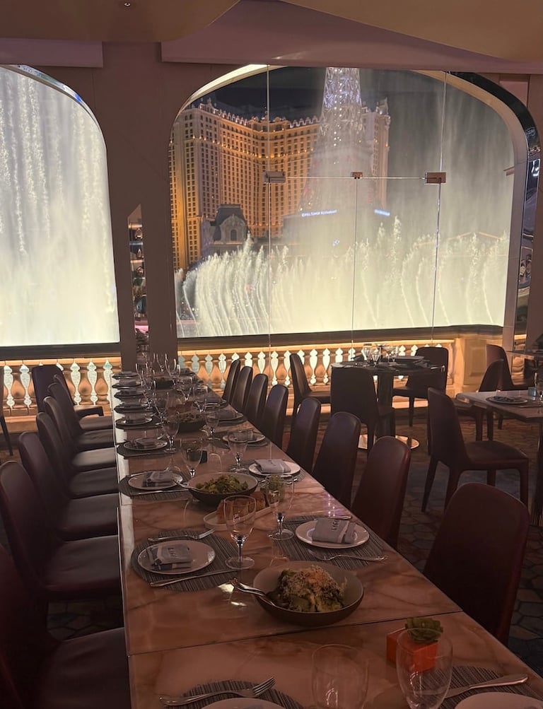 Fine dining restaurant with large window overlooking illuminated fountain and casino building at night