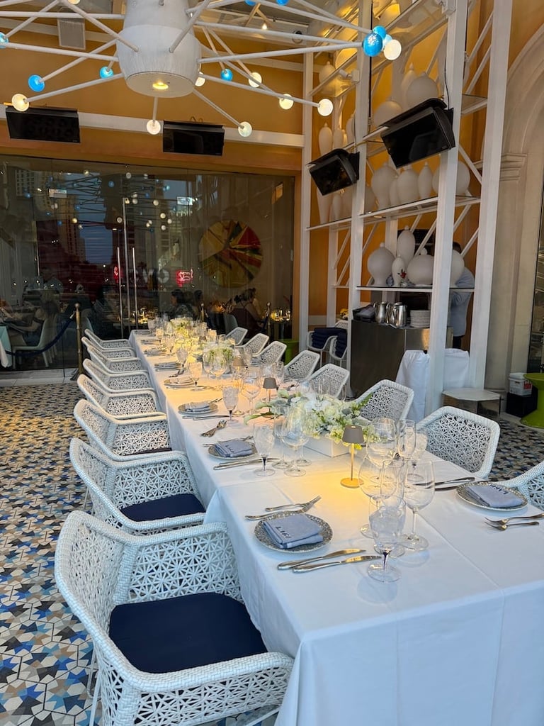 Long formal banquet table with white lace chairs, place settings, and floral centerpieces under modern industrial ceiling with pendant lights